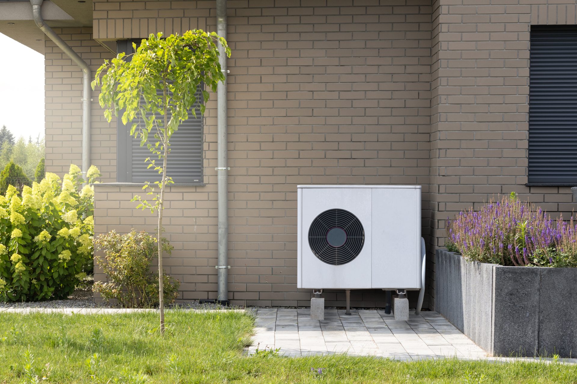 Wärmepumpen-Außengerät vor einem modernen Wohnhaus neben einem bepflanzten Hochbeet