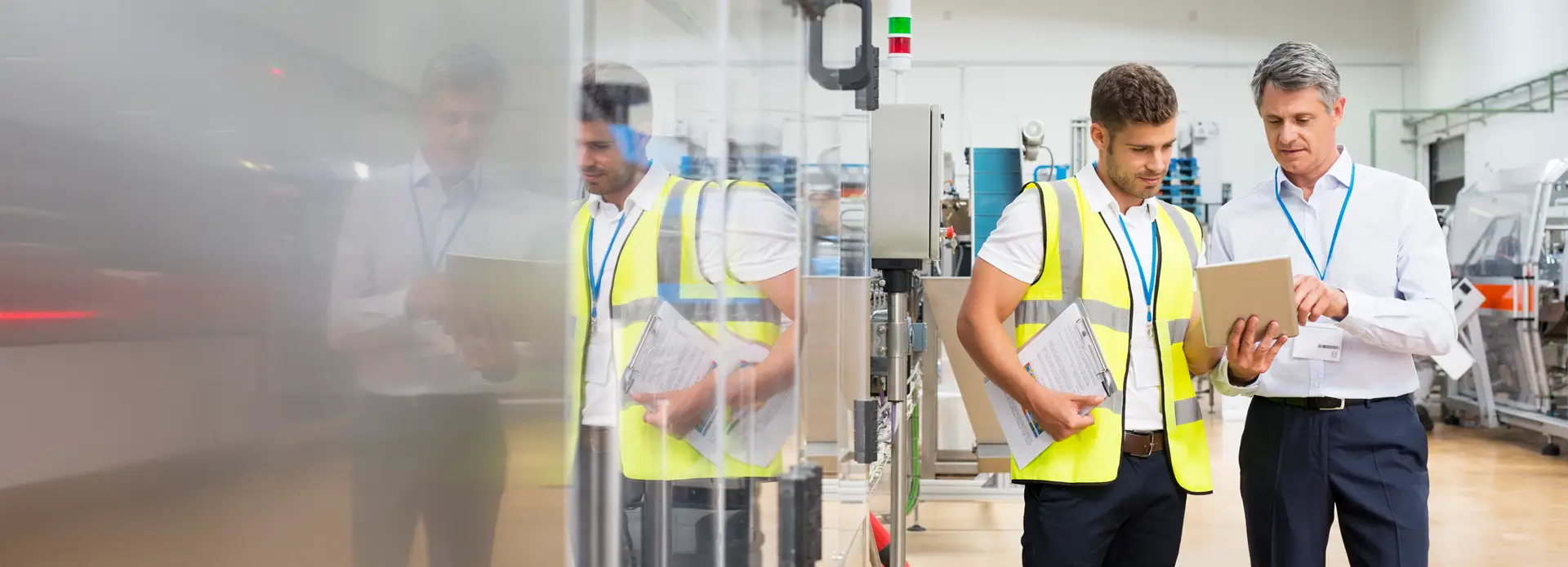Zwei Männer in einer Fabrikhalle betrachten gemeinsam ein Tablet und besprechen sich.