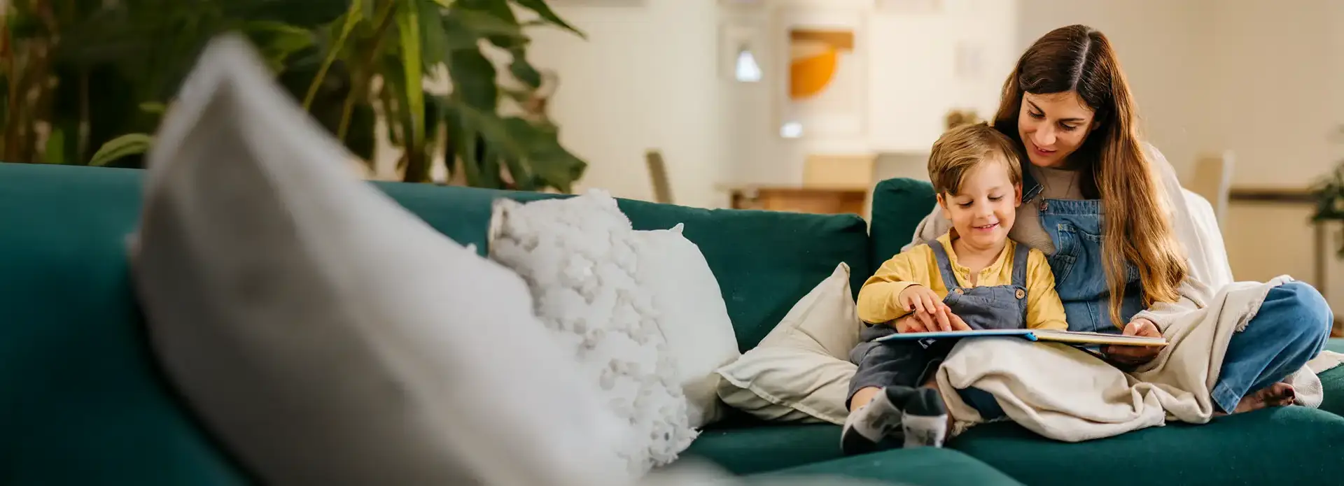 Mutter liest mit ihrem kleinen Sohn auf dem Sofa ein Buch in gemütlicher Wohnzimmeratmosphäre